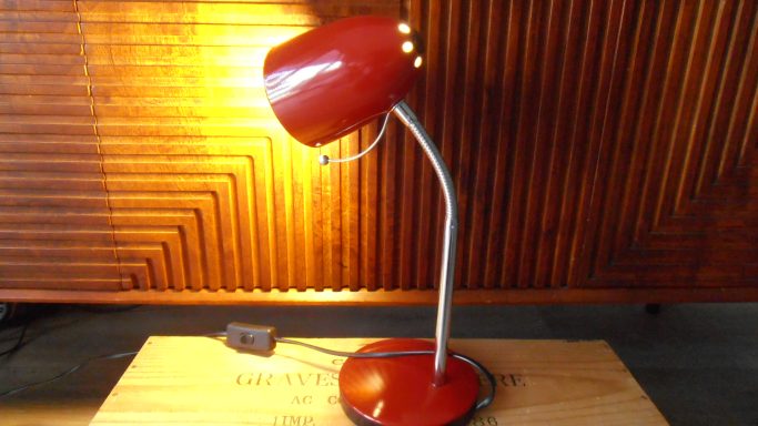 Rode bureaulamp met een gebogen arm en warm licht, naast een houten achtergrond.