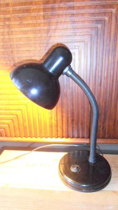 Zwarte bureaulamp met een gebogen arm en ronde basis op een houten tafel.