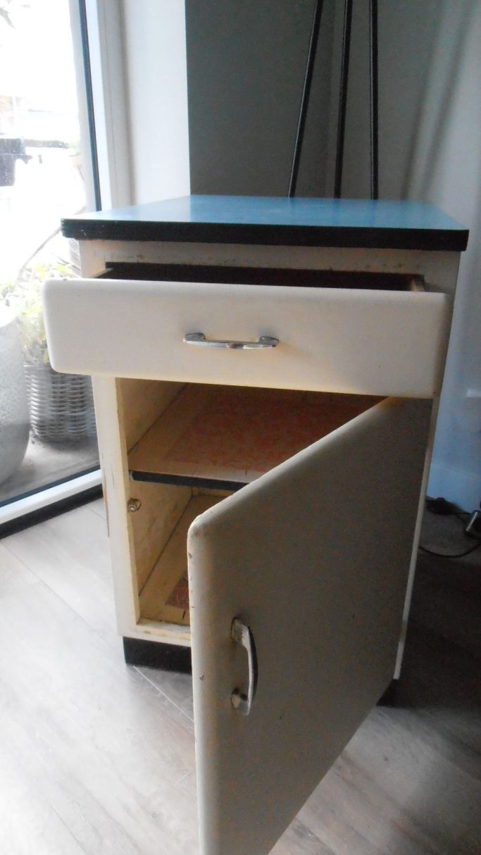 Kast met een lade en een open deur, op een houten vloer bij een raam.