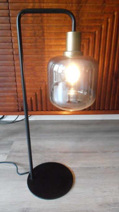 Moderne vloerlamp met een glazen kap en een gouden fitting op een zwarte basis.